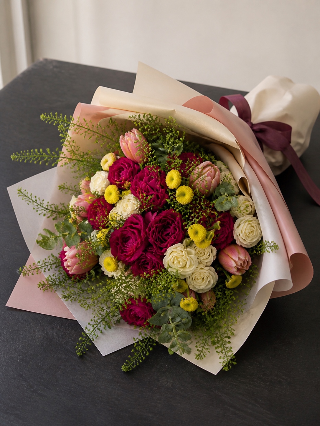 Magenta, yellow, and white bouquet in Korean-inspired wrapping laid flat on a black table